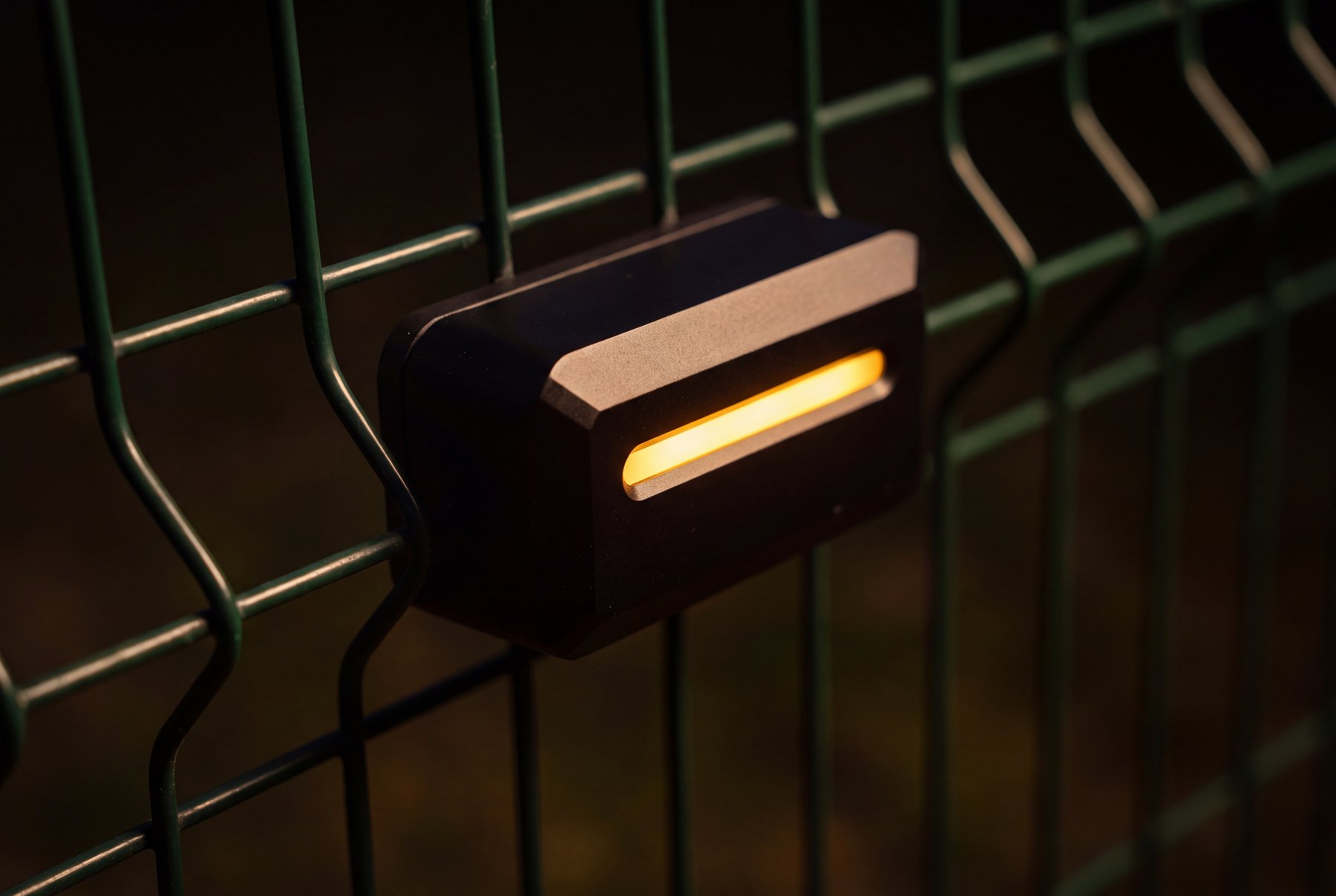 A re-engineered GPSX sensor on fence mesh at night, its amber line glowing.